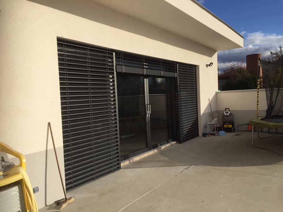 De grandes portes coulissantes en verre recouvertes de stores extérieurs horizontaux à lattes noires.