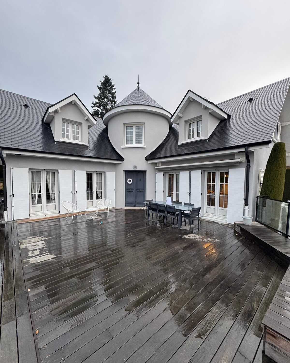 Une maison grise avec une tourelle centrale et des volets blancs.