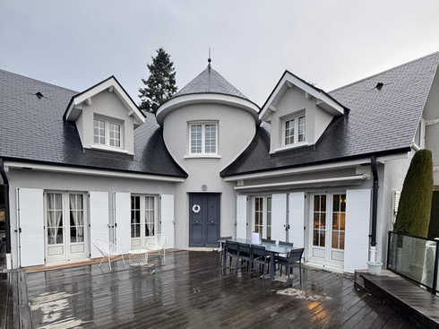 Une maison gris clair à deux étages avec des volets blancs.