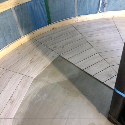 Vaaleat puujäljitelmälaudat asennetaan säteittäiseen kuvioon betonilattialle pyöreän rakenteen sisään.