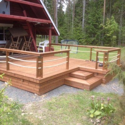Puinen kansi, jossa on köysikaiteet ja punainen mökki metsäisessä ympäristössä.