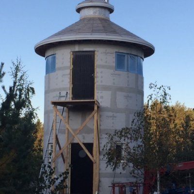 Rakenteilla oleva sylinterimäinen torni, jossa on harmaat tiiliseinät, kartiomainen katto, kaksi ovitasoa ja puinen rakennusteline.