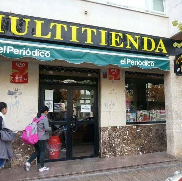 Fachada de un local con toldo verde y dos personas entrando; probablemente se trate de una tienda de conveniencia o un quiosco de periódicos.