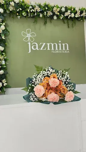 Ramo de flores naranjas y rosas sobre una superficie blanca, delante de una pared verde con el logotipo de una floristería.