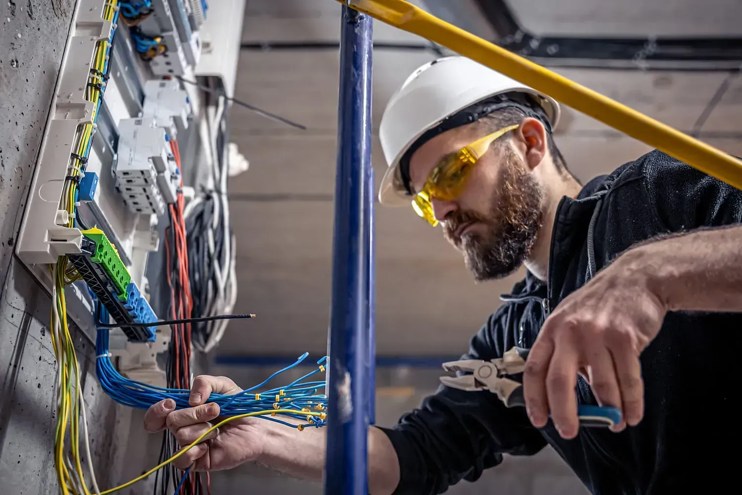 Electricista con casco y gafas de seguridad trabajando en el cableado.