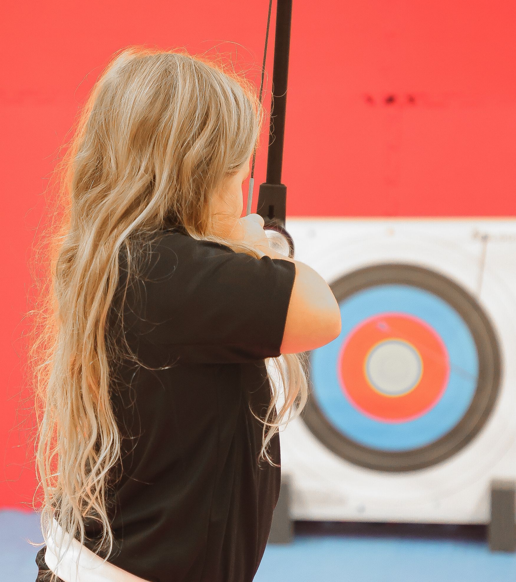 Eine Person zielt mit Pfeil und Bogen auf eine Zielscheibe mit roten, weißen und blauen Ringen.