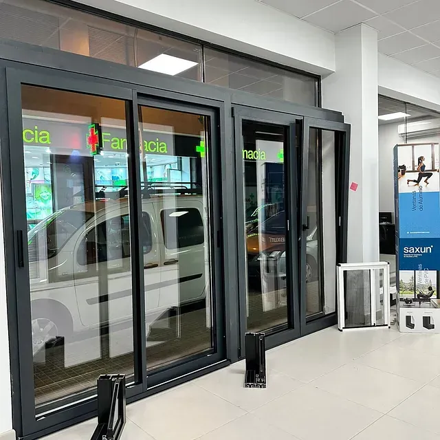 Una farmacia con puertas corredizas de vidrio y una camioneta blanca estacionada frente a ella.