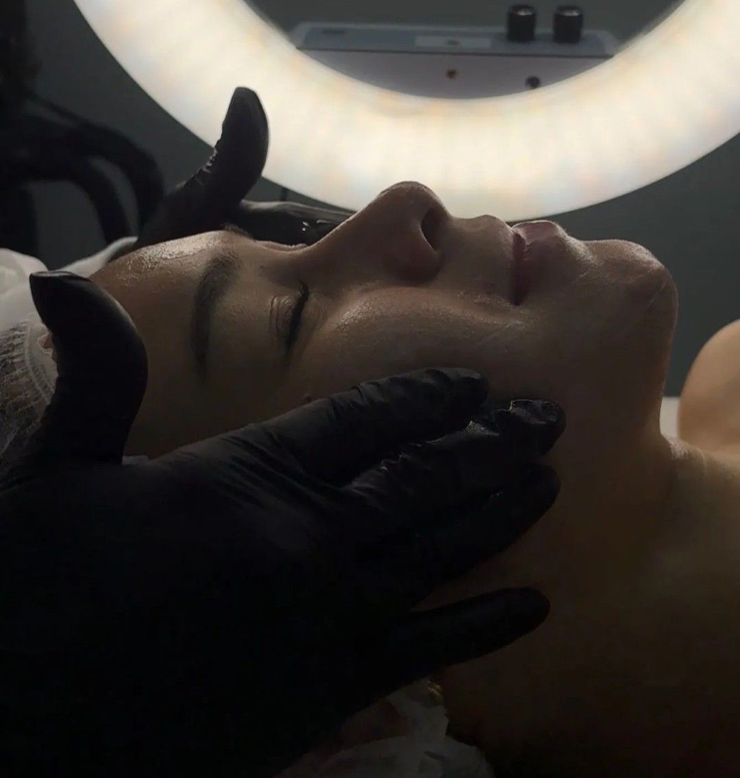 Tratamiento facial en curso, con unas manos enguantadas ajustando la mandíbula de un cliente bajo un aro de luz
