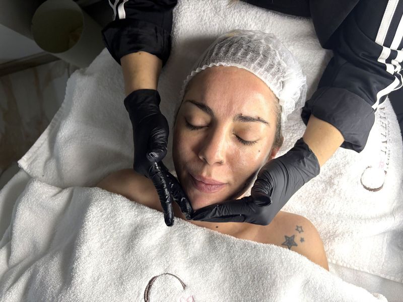Tratamiento facial en un spa, con una esteticista masajeando el rostro de una clienta en una camilla de tratamiento