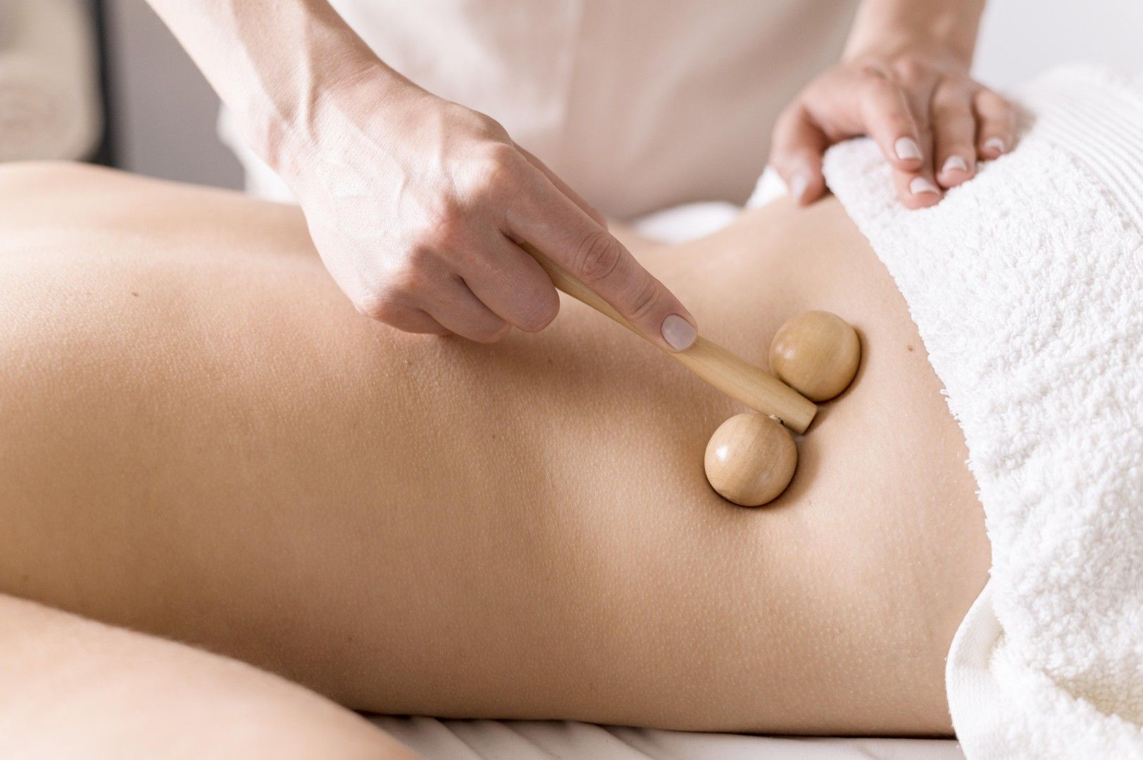 Manos que utilizan piedras de masaje de madera sobre la espalda desnuda de una persona durante un tratamiento de spa