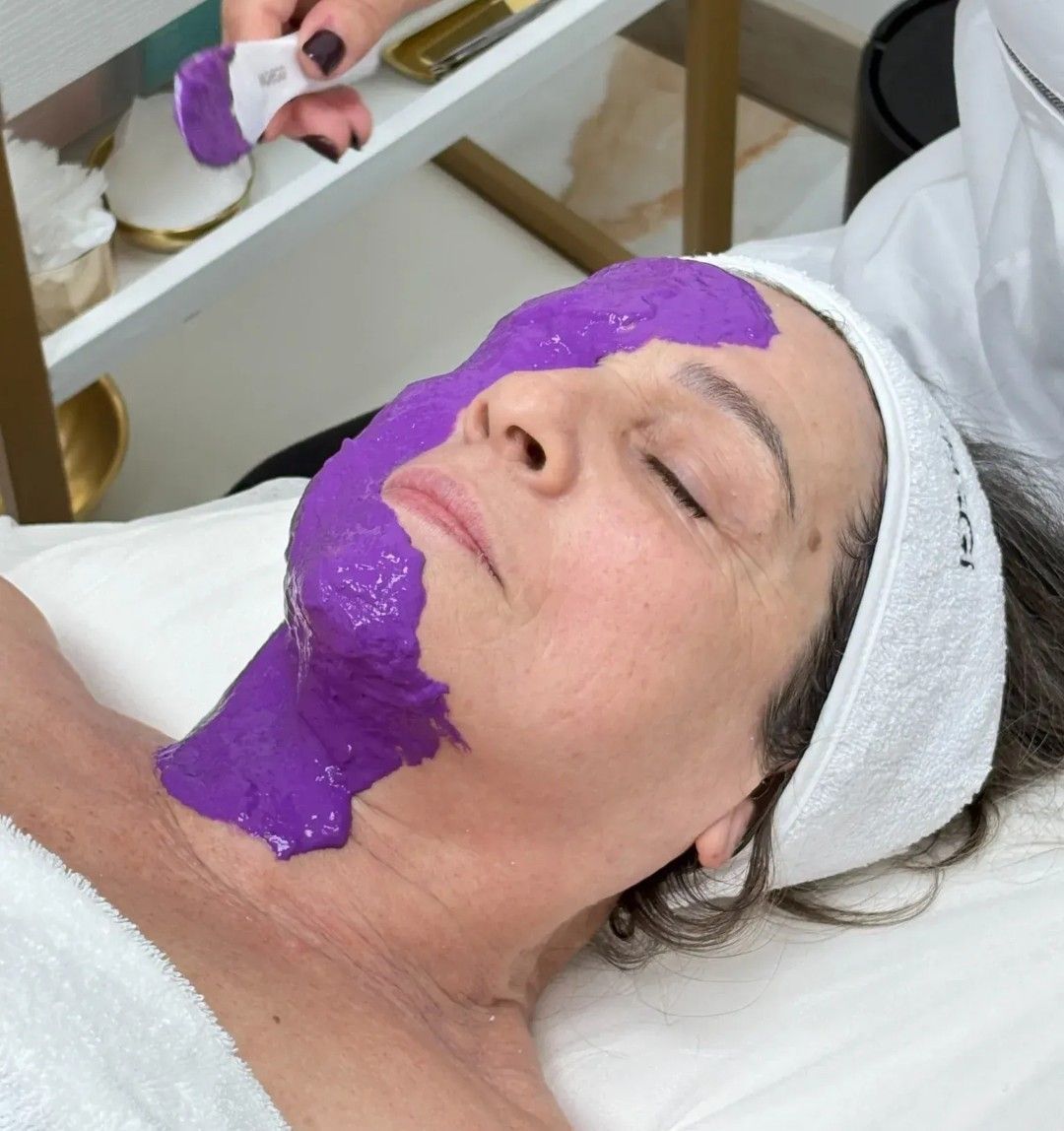 Mujer recibiendo una mascarilla facial morada en una sala de tratamientos de spa