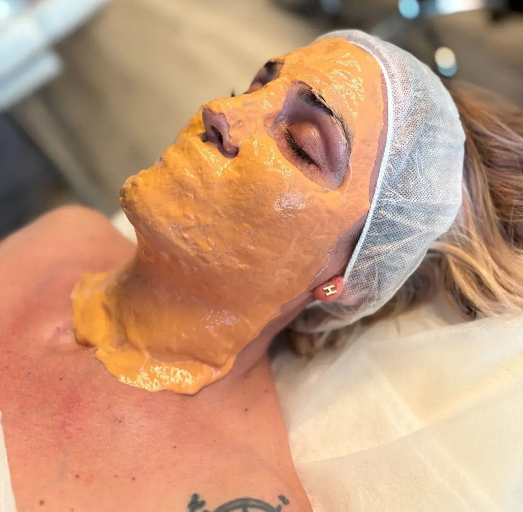 Mujer a la que le aplican una mascarilla facial amarilla durante un tratamiento de spa, recostada con los ojos cerrados.