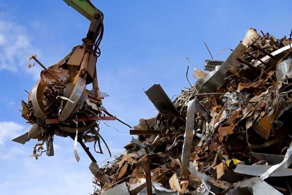 Una grúa de garra levantando chatarra contra un cielo azul.