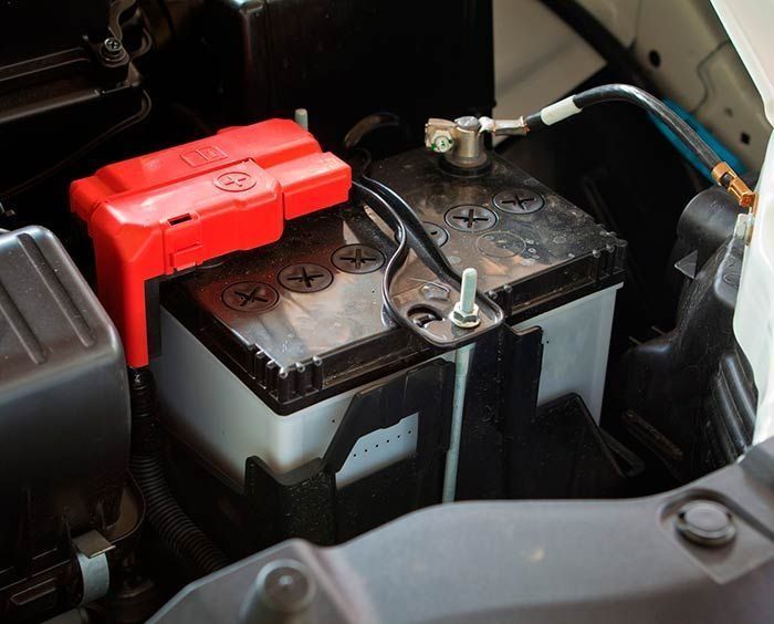 Batería de automóvil en el compartimiento del motor de un vehículo; negro, gris, rojo y blanco.