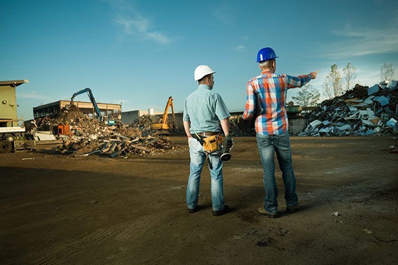 Dos trabajadores de la construcción con cascos inspeccionan un sitio de construcción con escombros.