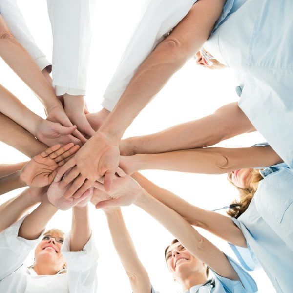 Profesionales médicos, brazos levantados, manos unidas en círculo, mostrando trabajo en equipo y apoyo.