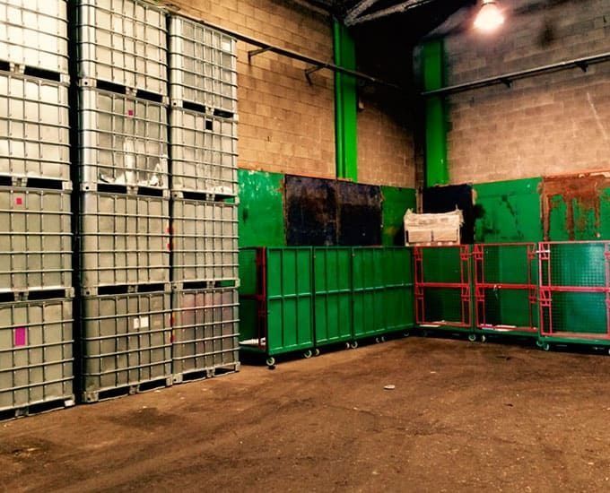 Interior de almacén con contenedores apilados y contenedores rodantes; verde y gris.
