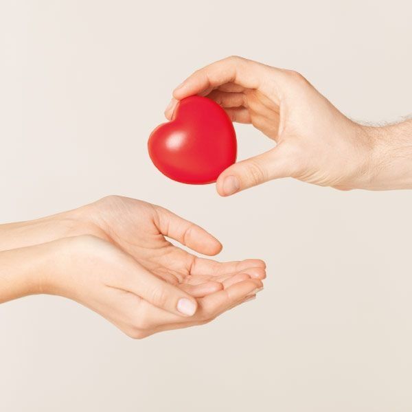 Manos intercambiando un corazón rojo, transmitiendo dar y recibir amor o cuidado.