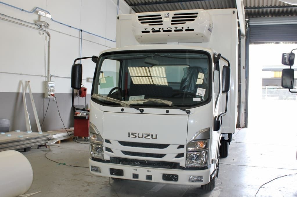 Camión Isuzu blanco estacionado dentro de una bahía de almacén con puerta trasera elevada.