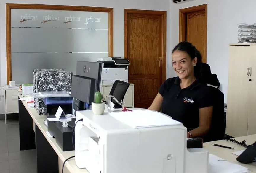 Empleado sonriente en una oficina con monitores de ordenador en una luminosa sala de oficinas.
