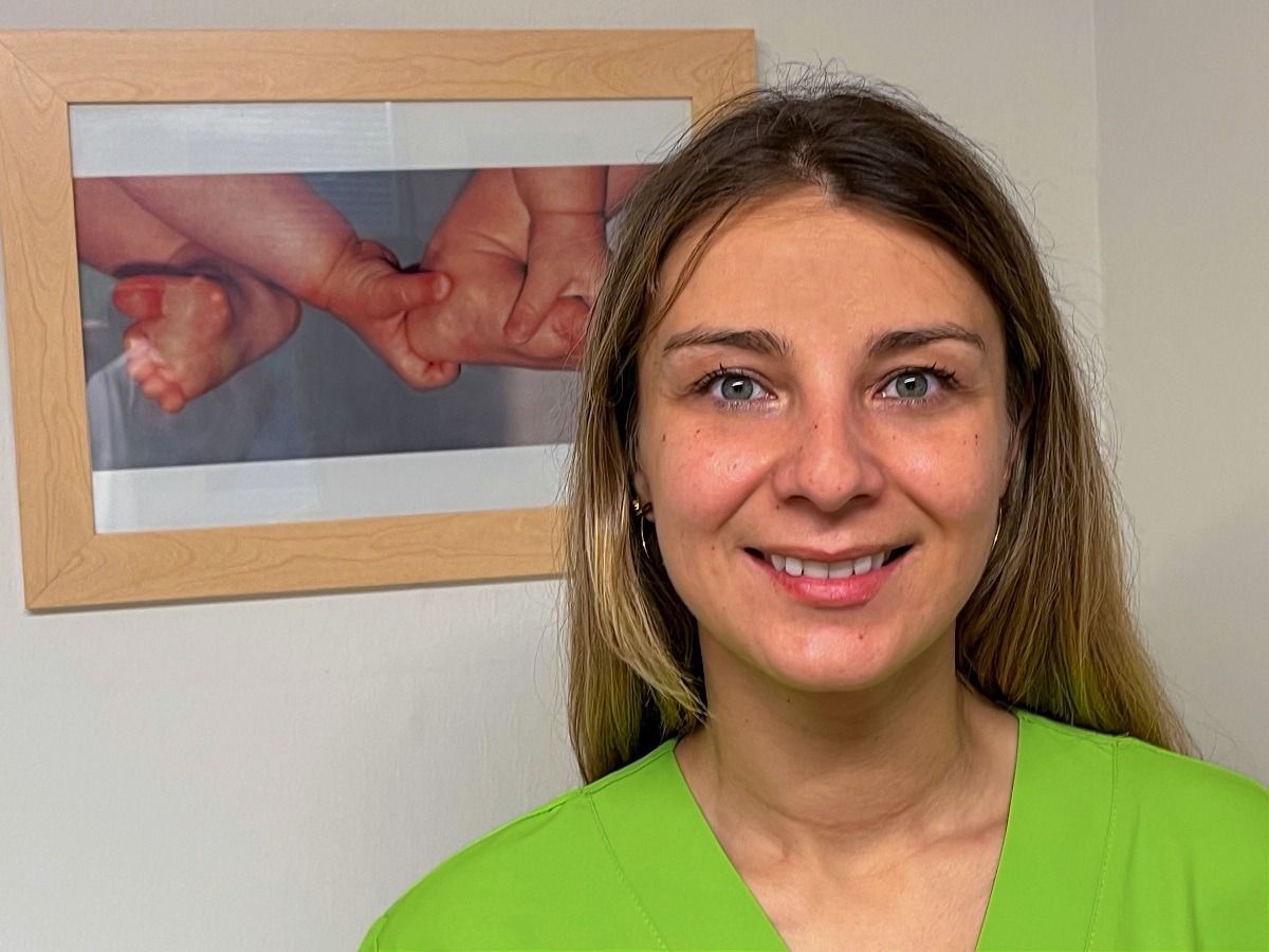 Una mujer con un uniforme verde sonríe delante de una foto de un bebé.