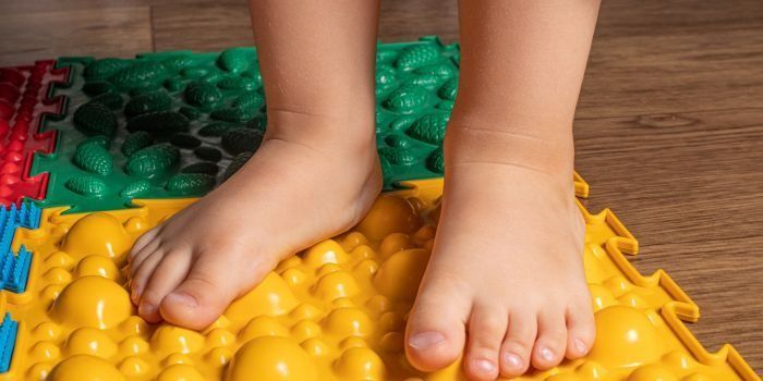 Los pies de un niño están parados sobre una alfombra amarilla.
