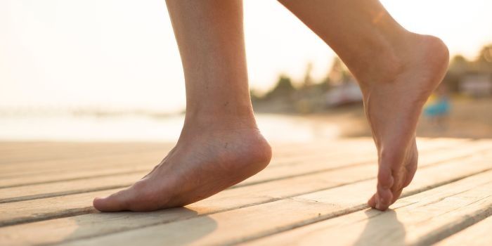 Los pies descalzos de una mujer caminan sobre un muelle de madera.