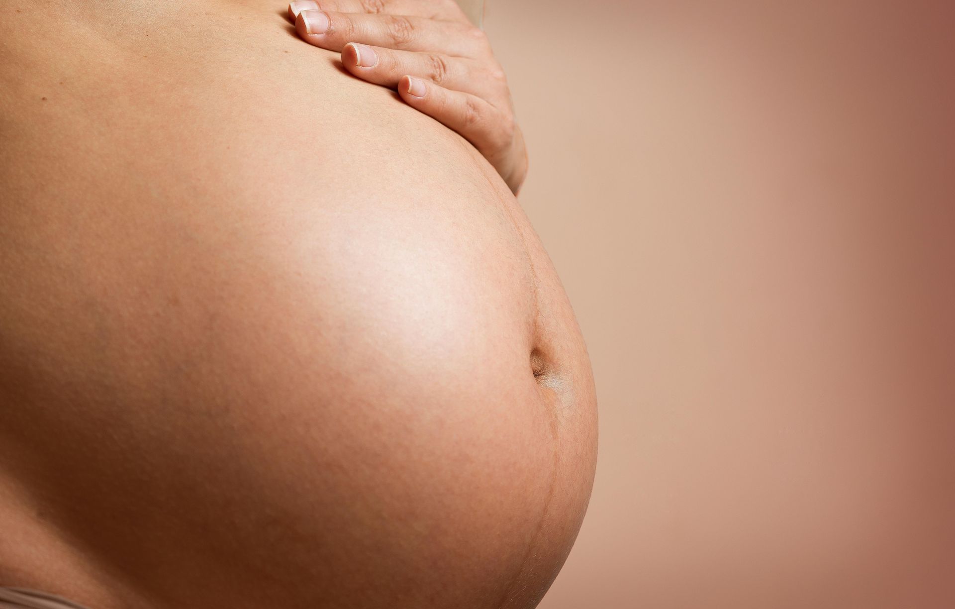Una mujer embarazada sostiene su vientre con sus manos.