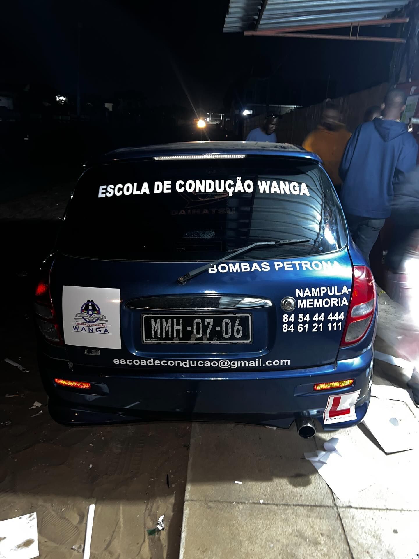 Carro azul de autoescola à noite com a placa e a inscrição “Escola de Condução Wanga” visíveis.