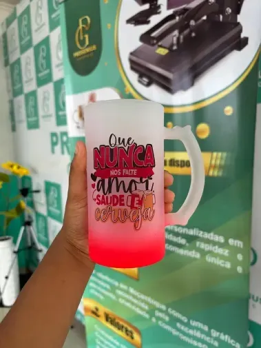Mão segurando uma caneca rosa degradê com letras pretas em frente a um fundo verde para exibição de produtos.