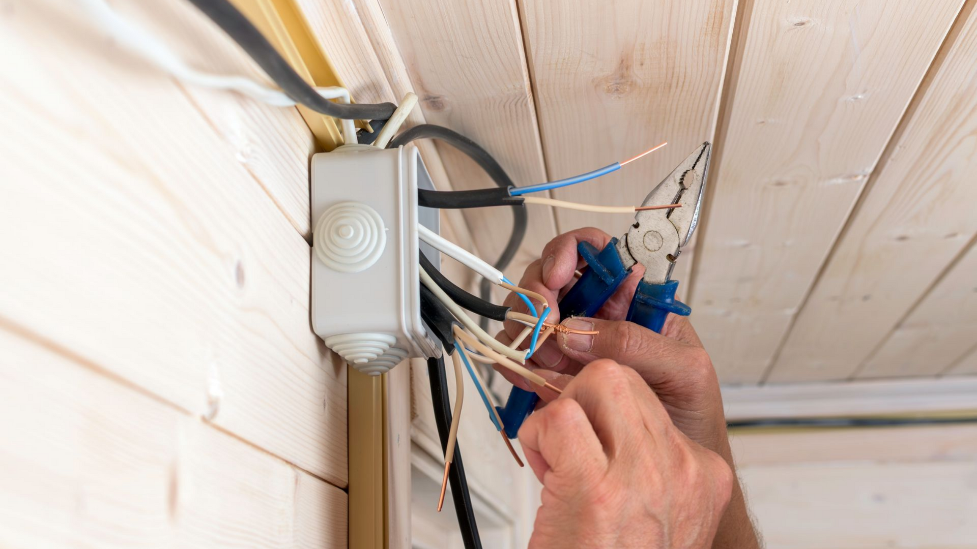 Raccordement manuel de fils électriques dans une boîte de jonction sous un plafond en bois.