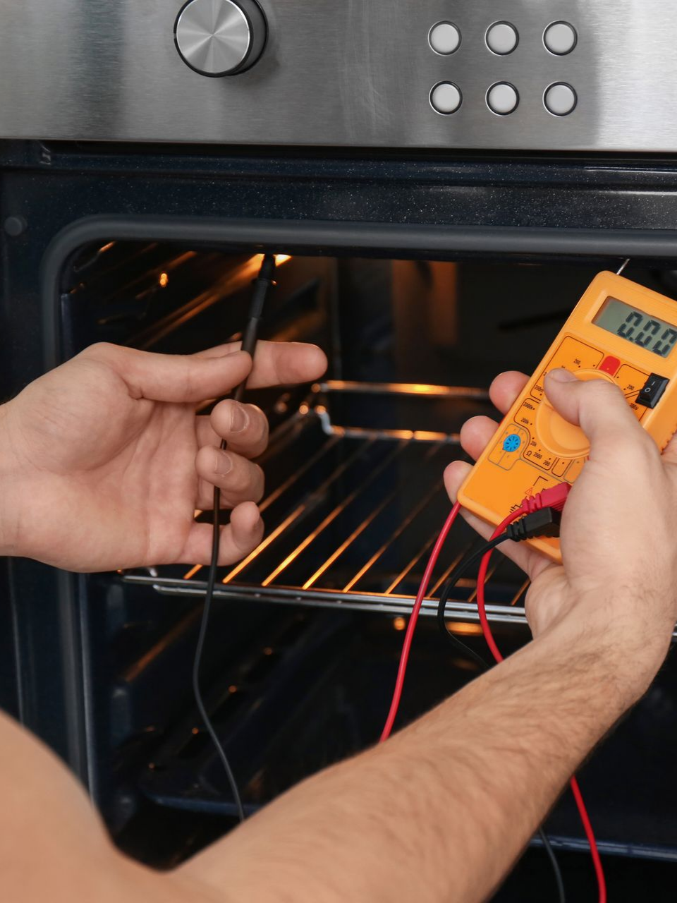 Des mains utilisent un multimètre pour tester l'intérieur d'un four.