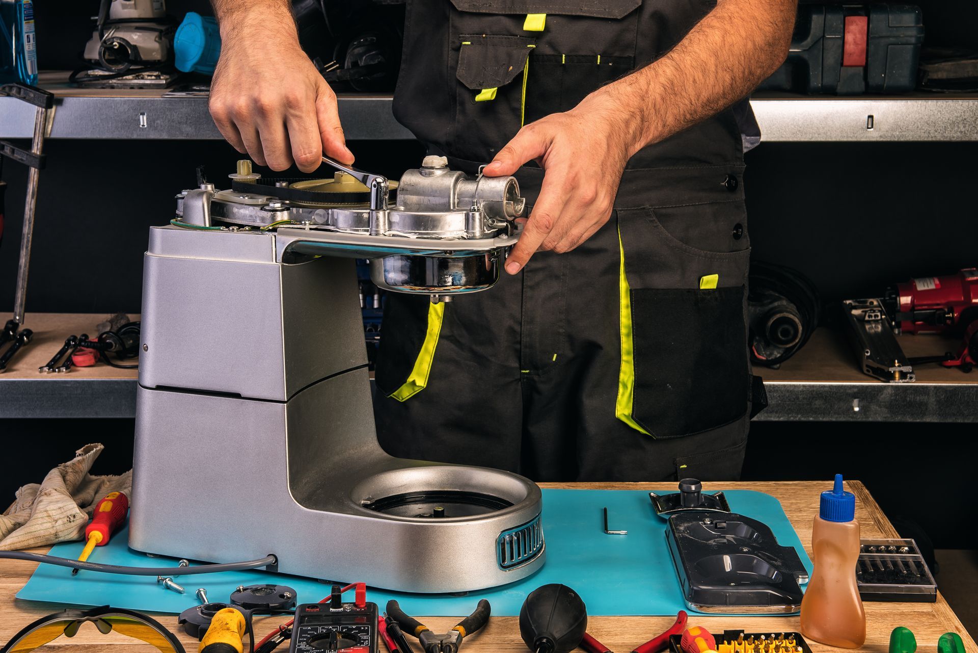Un technicien assemble une machine en métal gris sur un établi, entouré d'outils et de pièces détachées.
