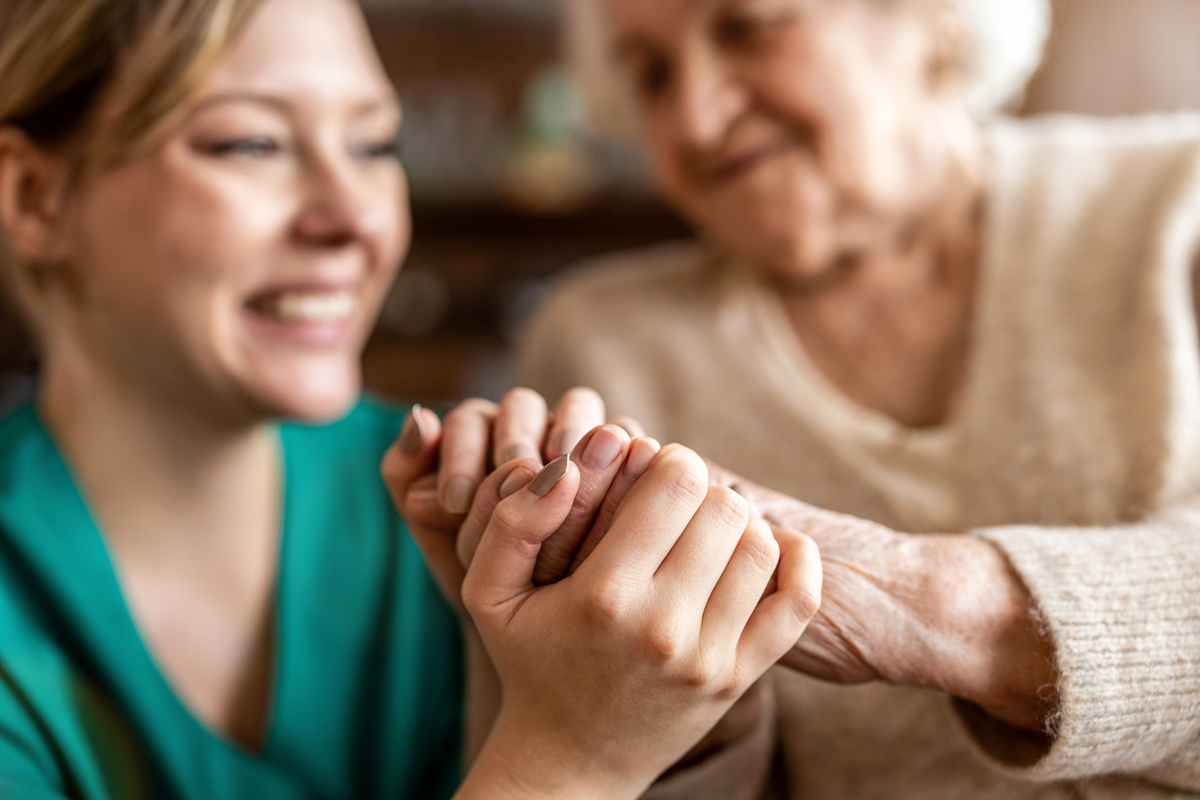 Aide-soignante souriante tenant les mains d'une personne âgée