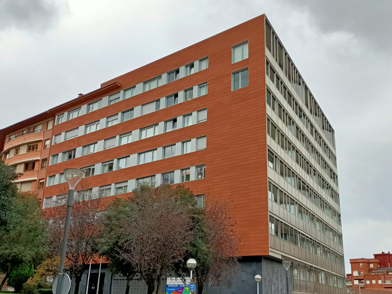 Un gran edificio de ladrillo con muchas ventanas está rodeado de árboles.
