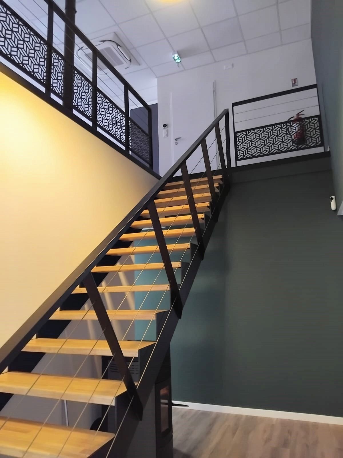 Escalier en bois avec supports en métal noir, sur fond de murs beiges et verts.