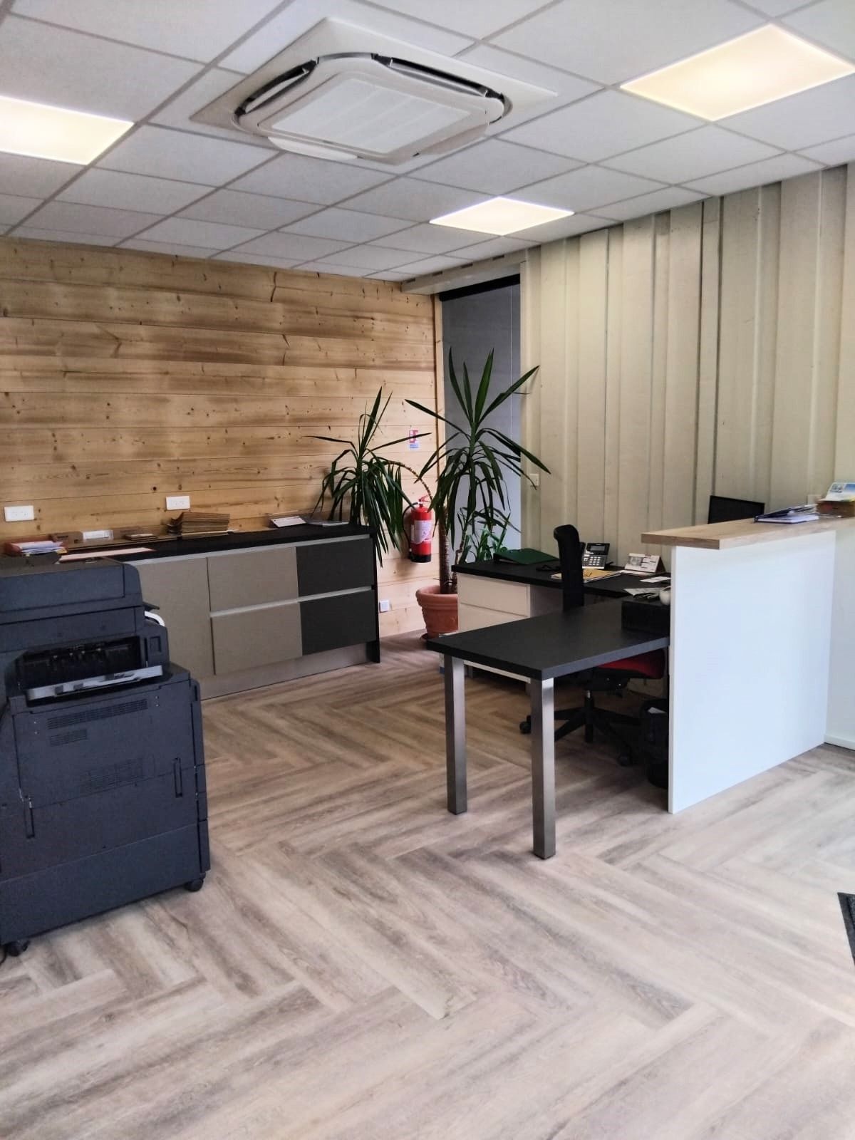 Bureau avec mur lambrissé, bureaux, imprimante, plantes et sol à chevrons.