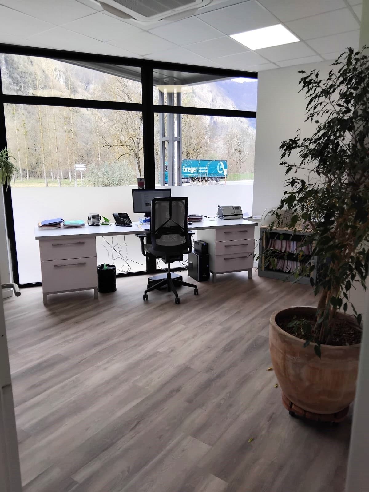 Intérieur de bureau avec bureau, chaise et plante, avec une grande fenêtre donnant sur un paysage avec des montagnes.