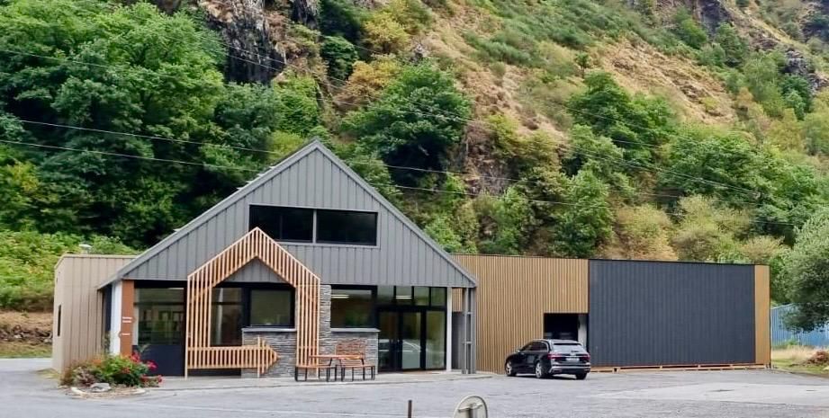 Bâtiment moderne avec bardage gris et bois dans un cadre montagneux, voiture garée à l'extérieur.