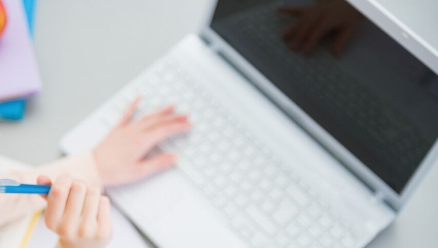 Manos tecleando en un teclado de portátil blanco con un bolígrafo cerca sobre un escritorio.