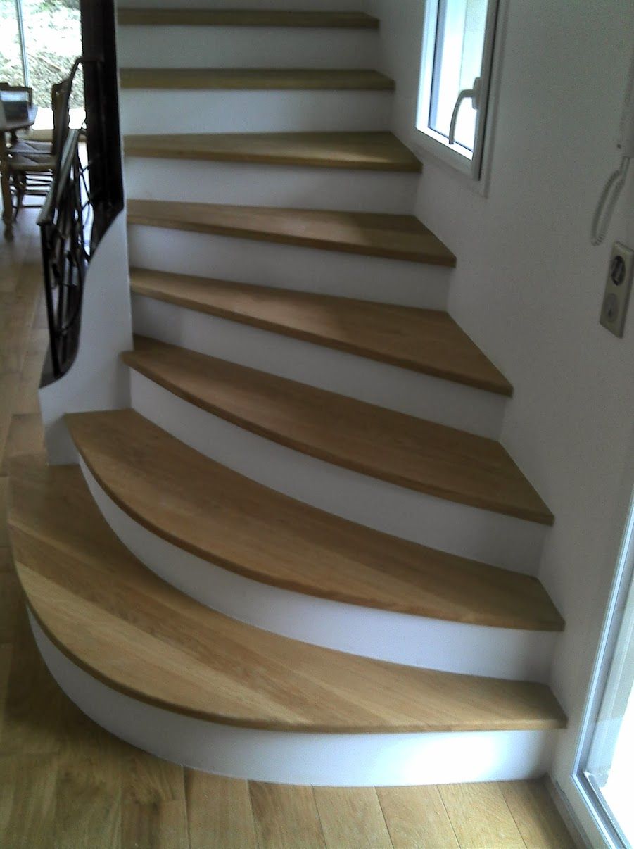 Escalier en bois où la lumière du soleil projette des ombres sur un mur blanc.