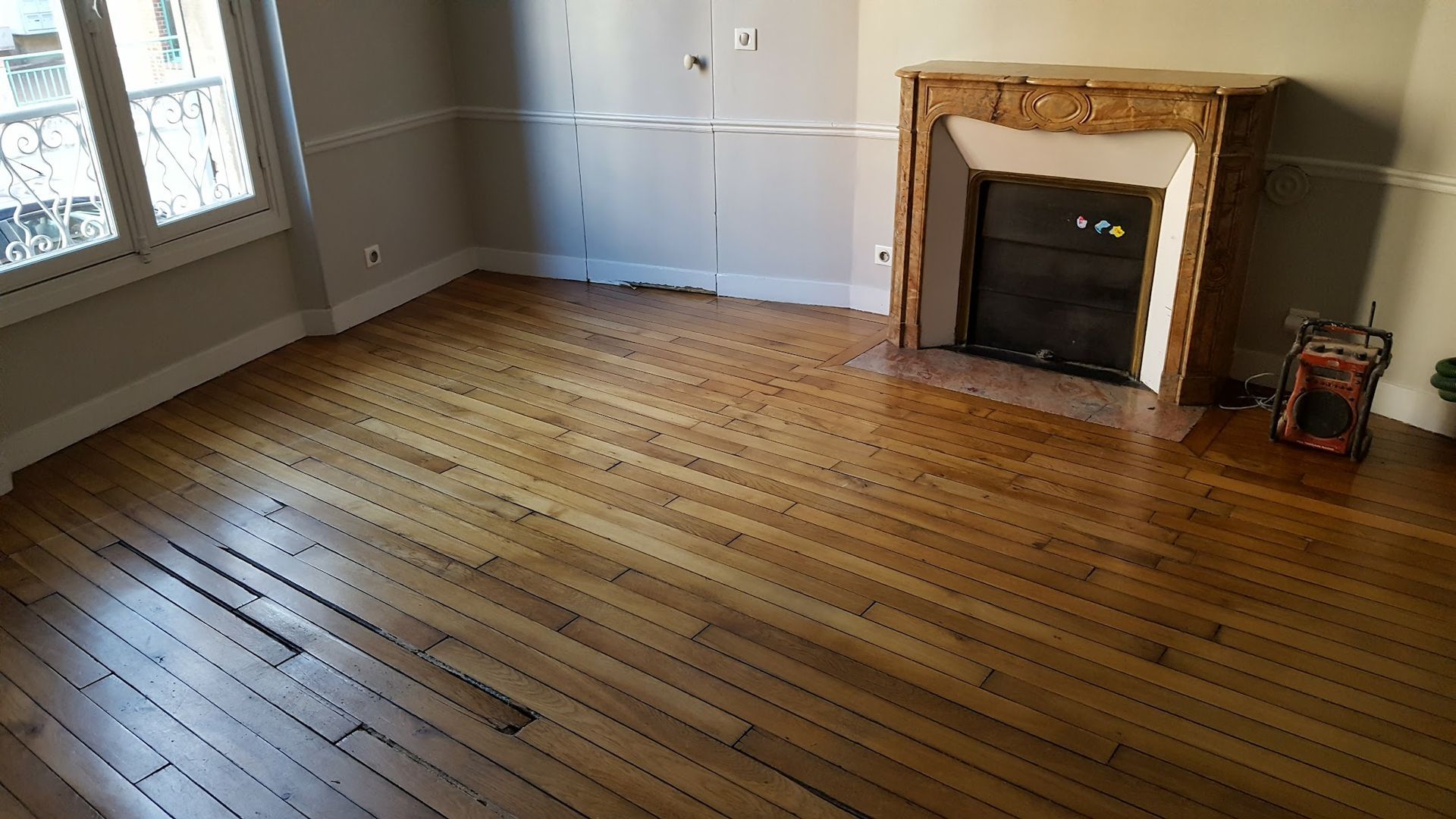 Sol en bois et cheminée dans une pièce avec fenêtre ; murs de couleur neutre.