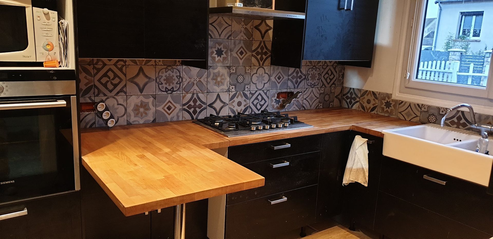 Une cuisine moderne avec des armoires noires, une crédence à motifs, un plan de travail en bois et une table pliante.