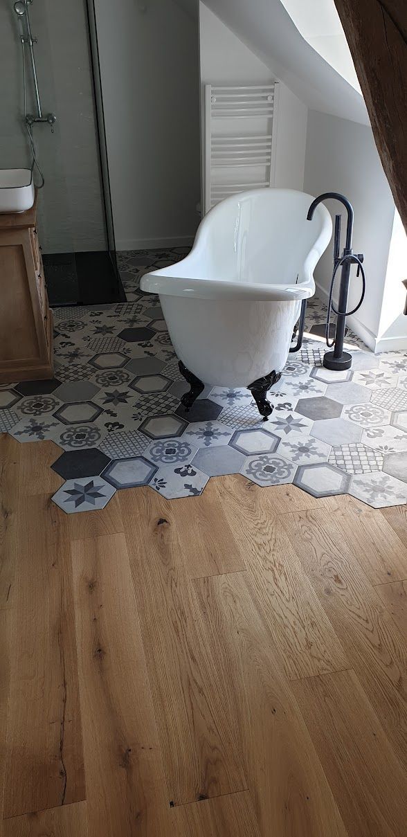 Salle de bains avec baignoire sur pieds, carrelage à motifs hexagonaux et parquet.