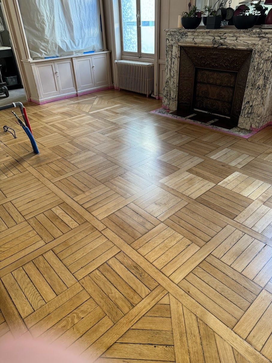 Sol en parquet dans une pièce, avec cheminée et fenêtre.