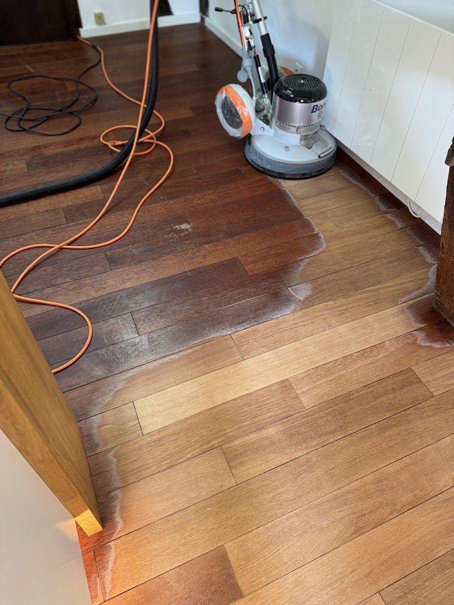 Rénovation du parquet à l'aide d'une polisseuse, montrant la transition entre une couleur de bois foncée et une couleur de bois plus claire.