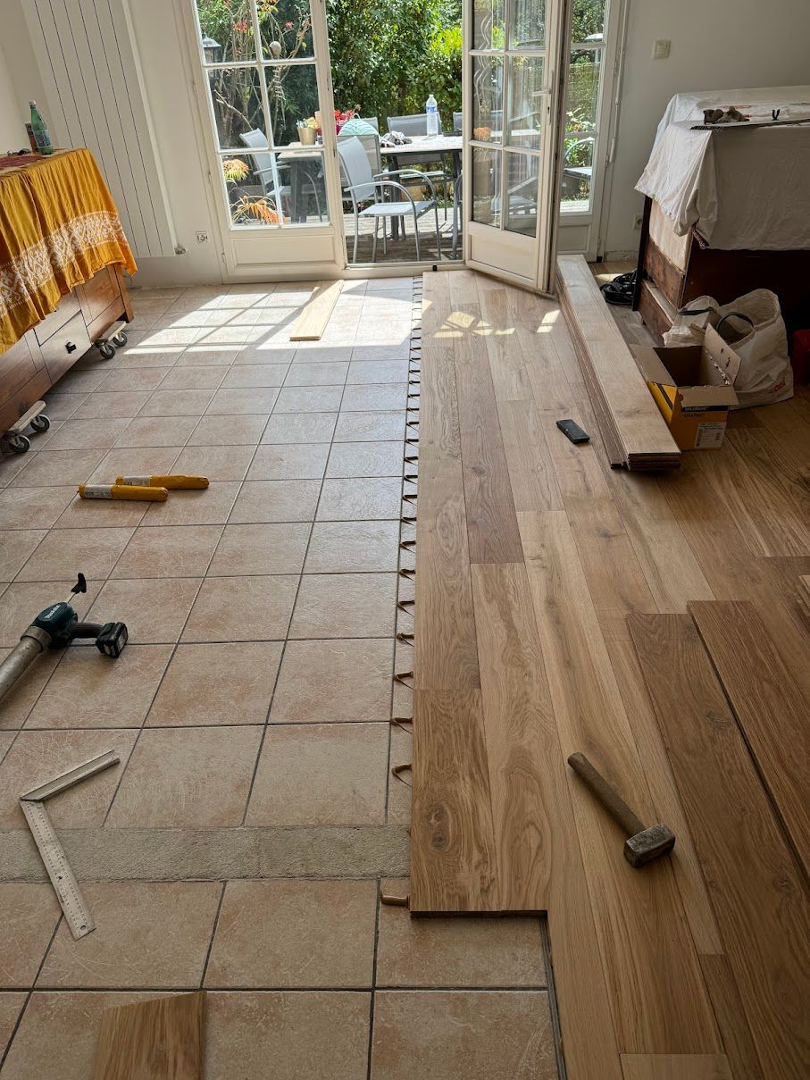 Pose de revêtement de sol : Des lames de parquet sont posées à côté d'un carrelage existant dans une pièce ensoleillée.