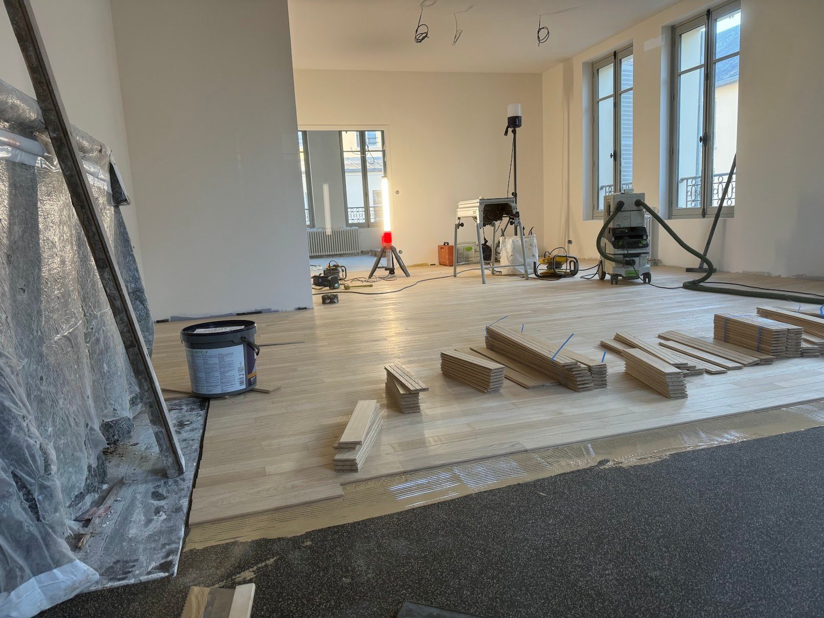 Intérieur avec pose de parquet en cours, outils et matériaux présents.