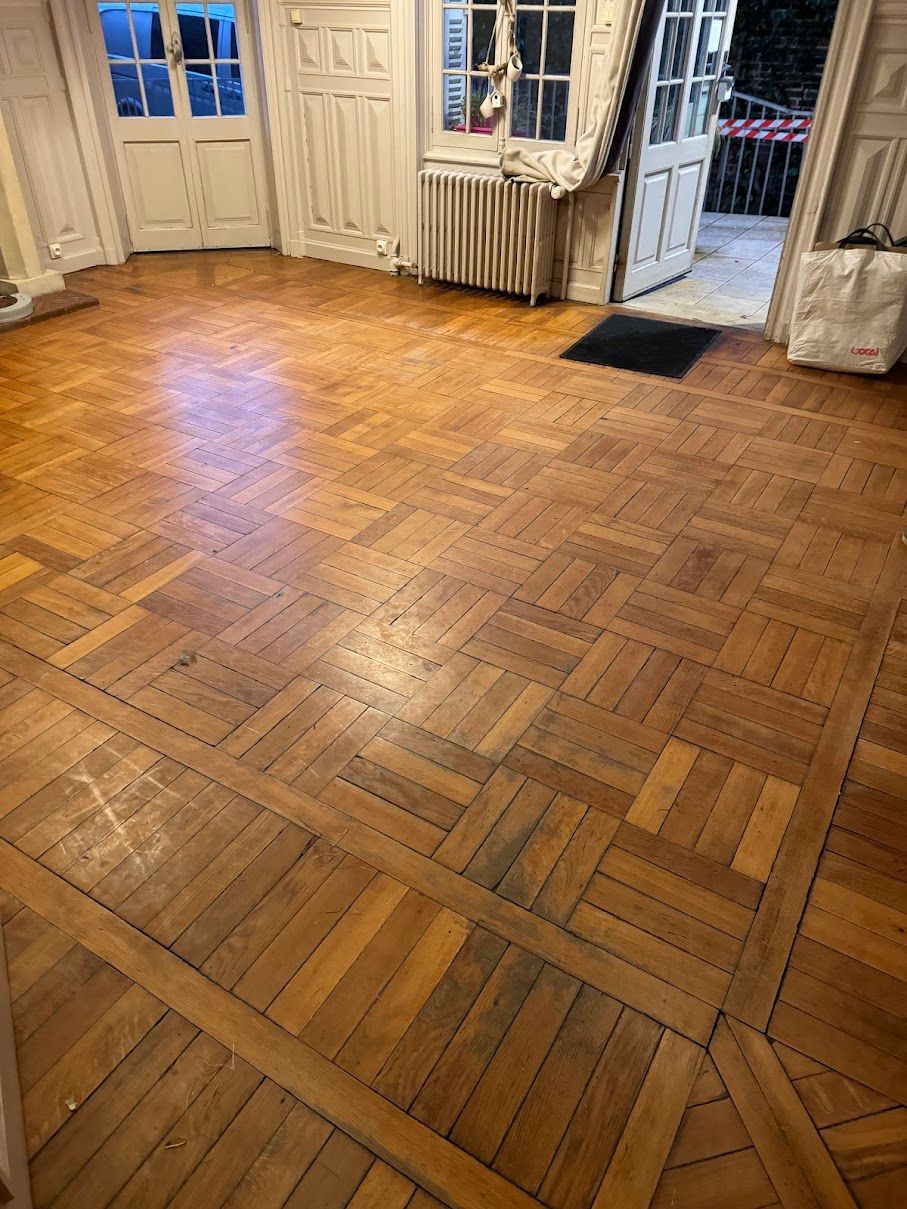 Sol en parquet dans une pièce, avec entrées et fenêtres visibles.