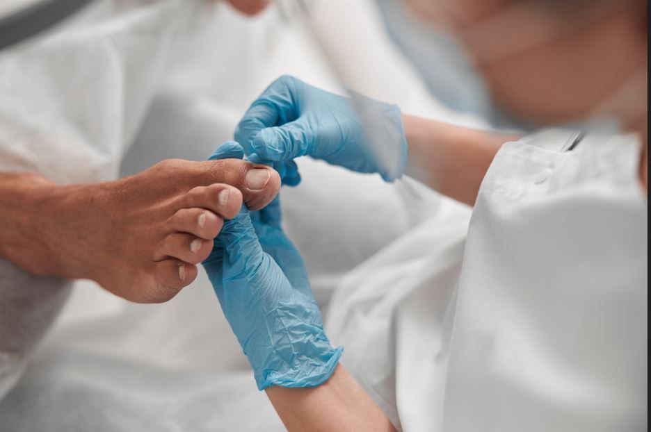 El pie de una persona siendo examinado por alguien que lleva guantes azules en un salón de belleza.